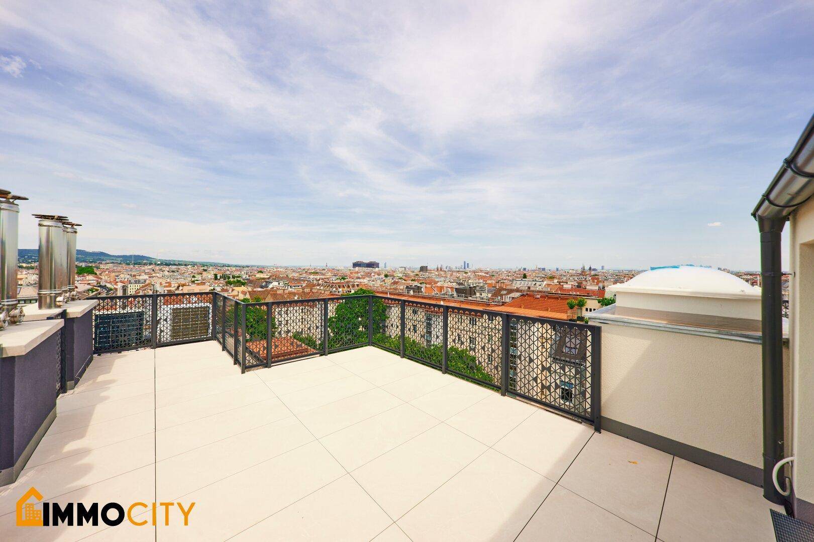 Weitläufige Dachterrasse mit Fliesenboden und Metallgeländer, bietet Panoramablick über die Stadt.