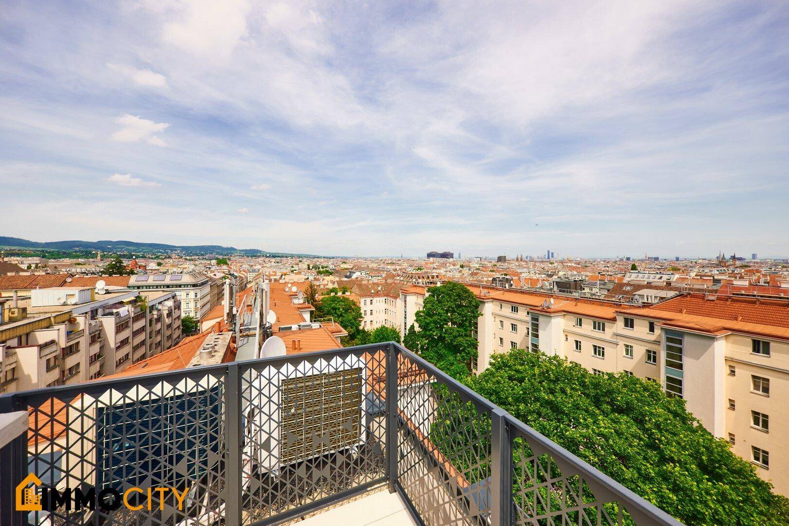 Dachterrasse mit modernem Geländer und weitem Blick über die Stadt und grüne Bäume.