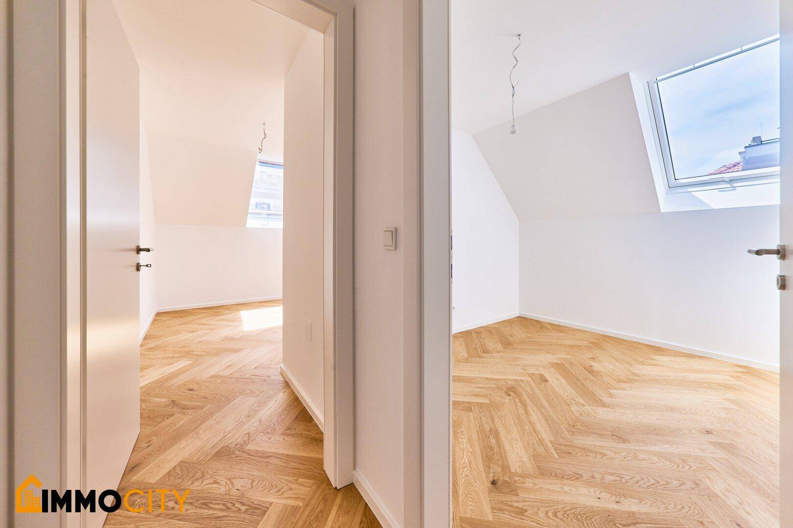 Heller Flurbereich mit Blick in zwei Zimmer im Dachgeschoss, ausgestattet mit Fischgrätparkett und Dachfenstern.