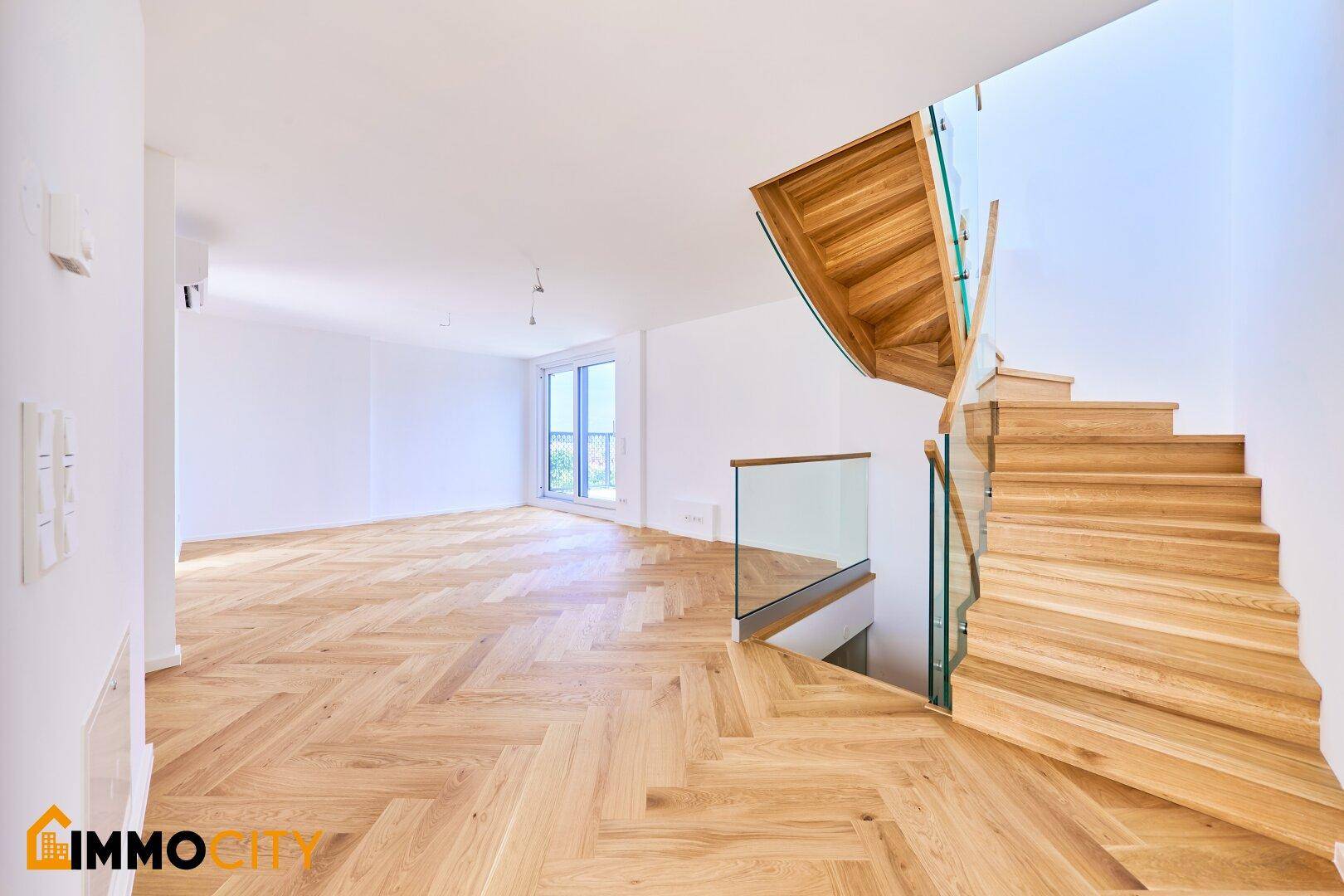 Eingangsbereich mit eleganter Holztreppe und Glasgeländer, offen gestaltet und hell.