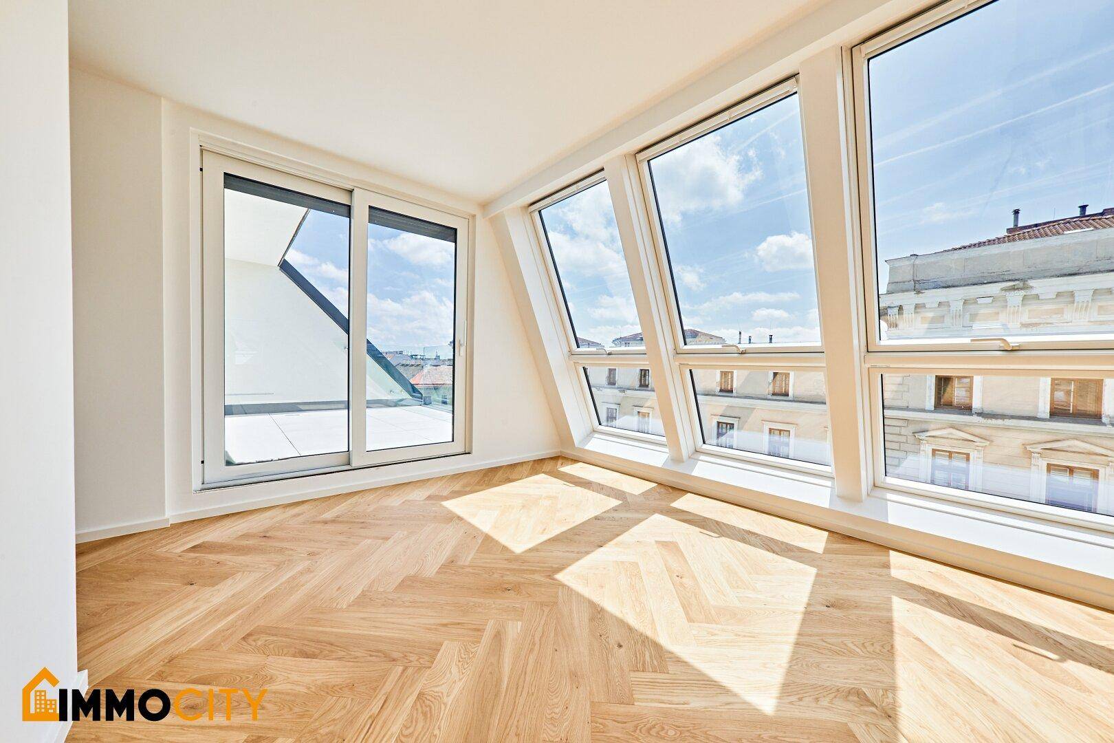 Heller Wohnraum mit Fischgrätparkett, großen Schrägfenstern und direktem Zugang zum Balkon.