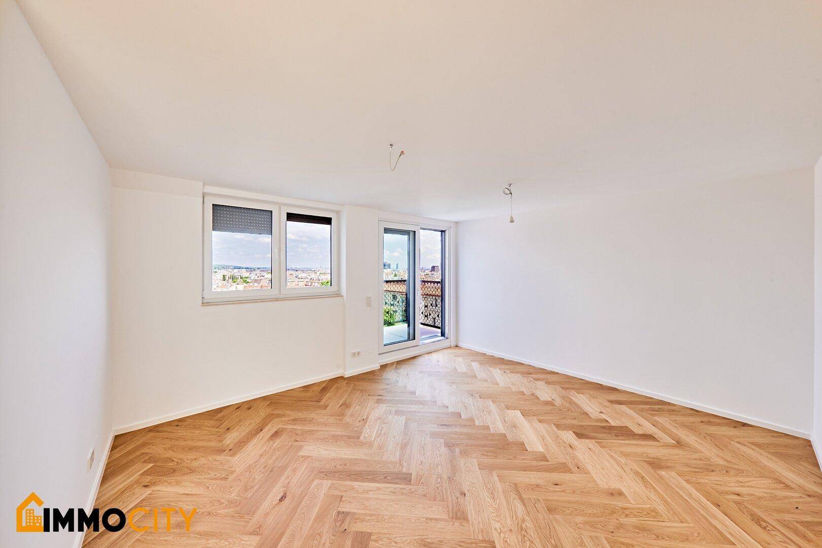 Helles Wohnzimmer mit Fischgrätparkett, Fenster mit Rollladen und Balkonzugang mit Stadtblick.