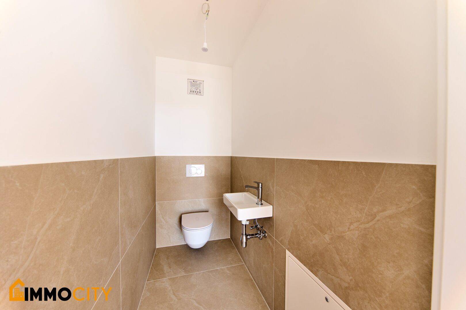 Modernes Gäste-WC mit beigefarbenen Fliesen, wandhängendem WC und kleinem Waschbecken.