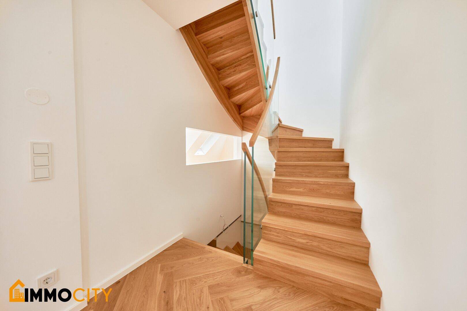 Elegante Holztreppe mit Glasgeländer, die verschiedene Ebenen des Hauses stilvoll verbindet.