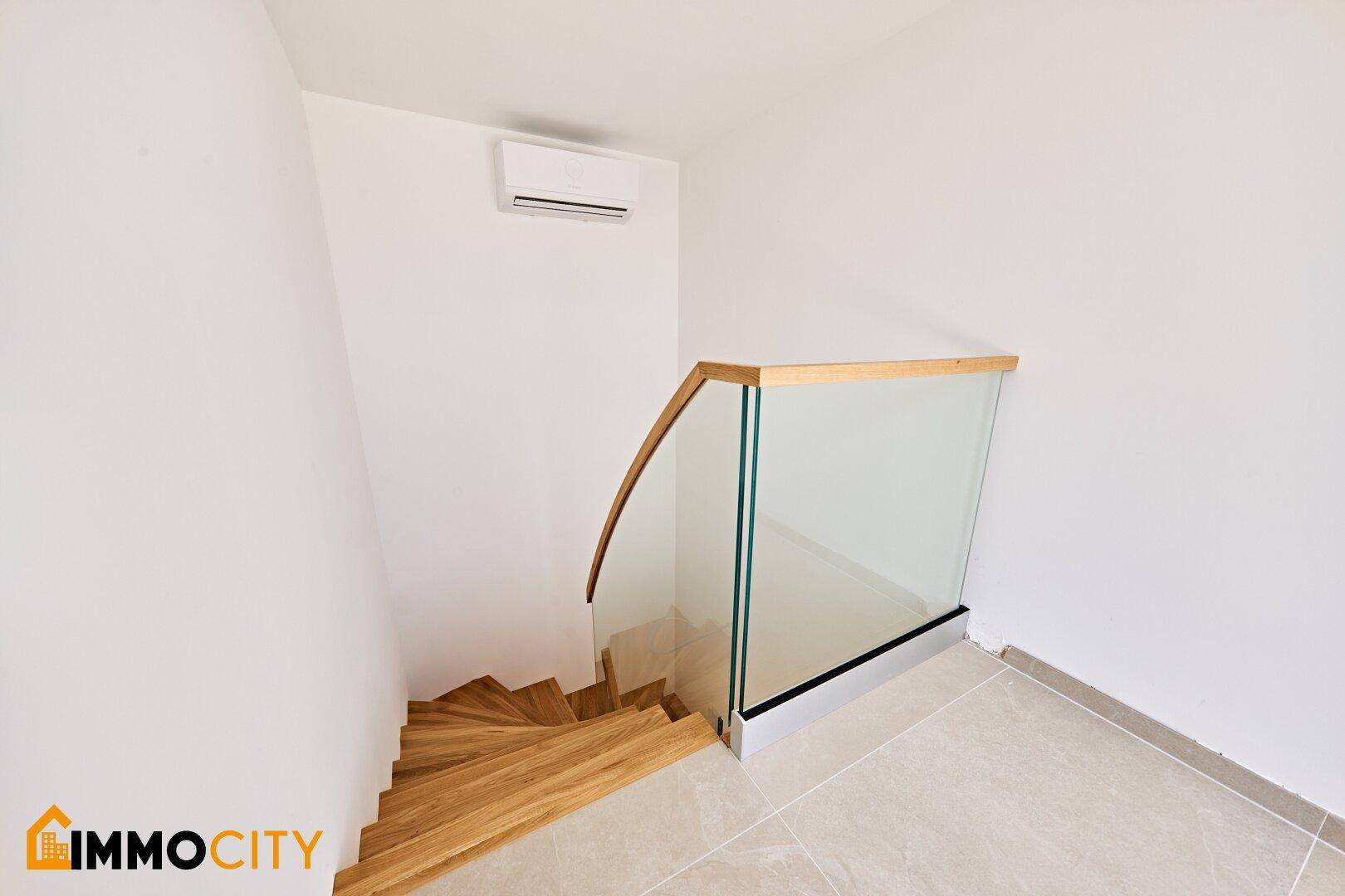 Oberer Treppenabsatz mit modernem Glasgeländer, Fliesenboden und Klimaanlage an der Wand.