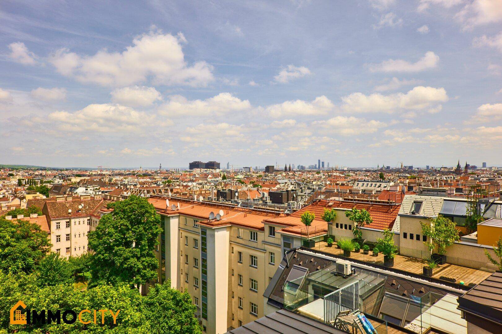 Weitläufiger Stadtblick von einem Balkon mit roten Dächern und blauem Himmel.
