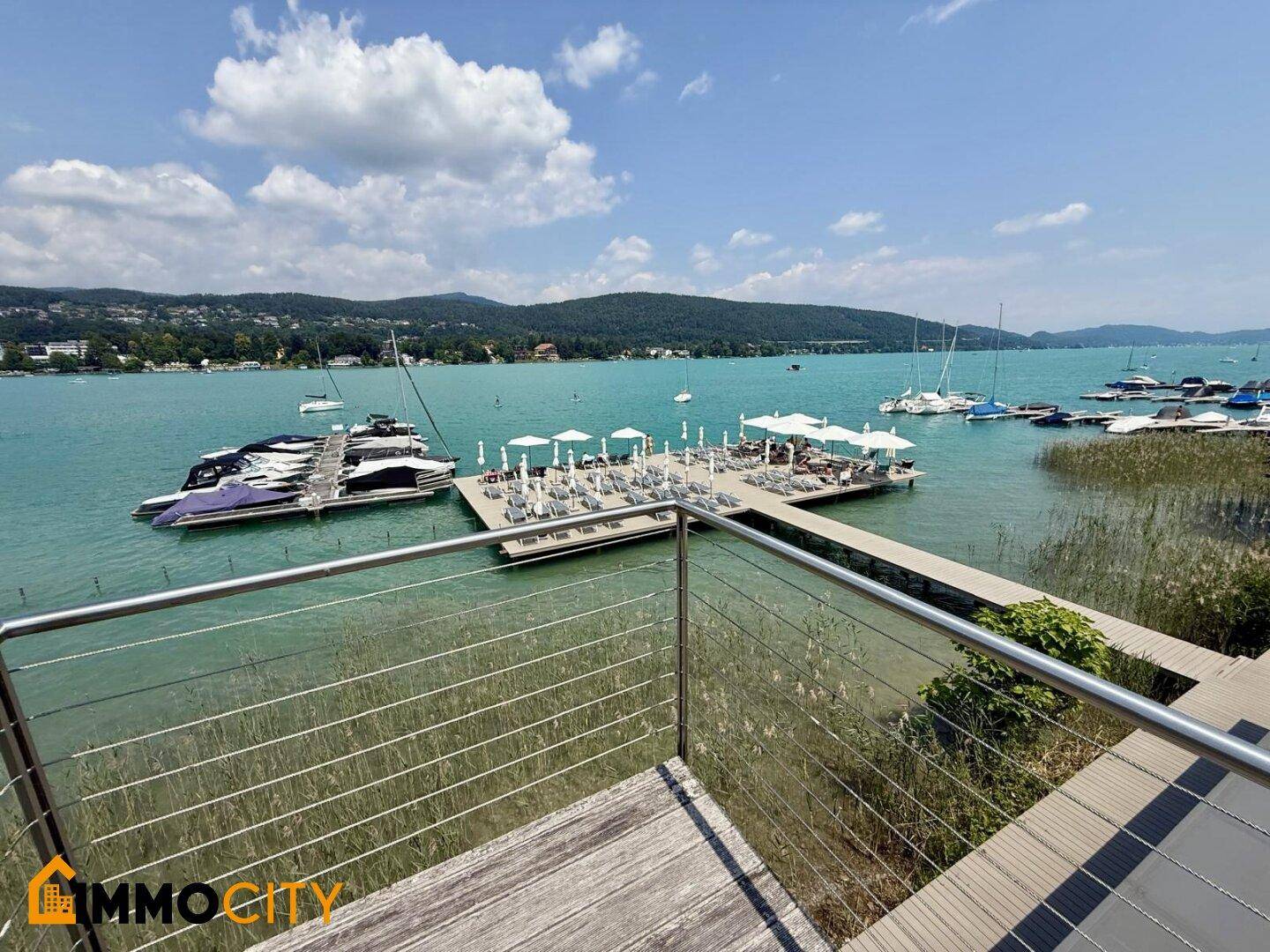 Panoramablick von einem Balkon auf den See mit Badestegen, Sonnenliegen und vielen Booten.