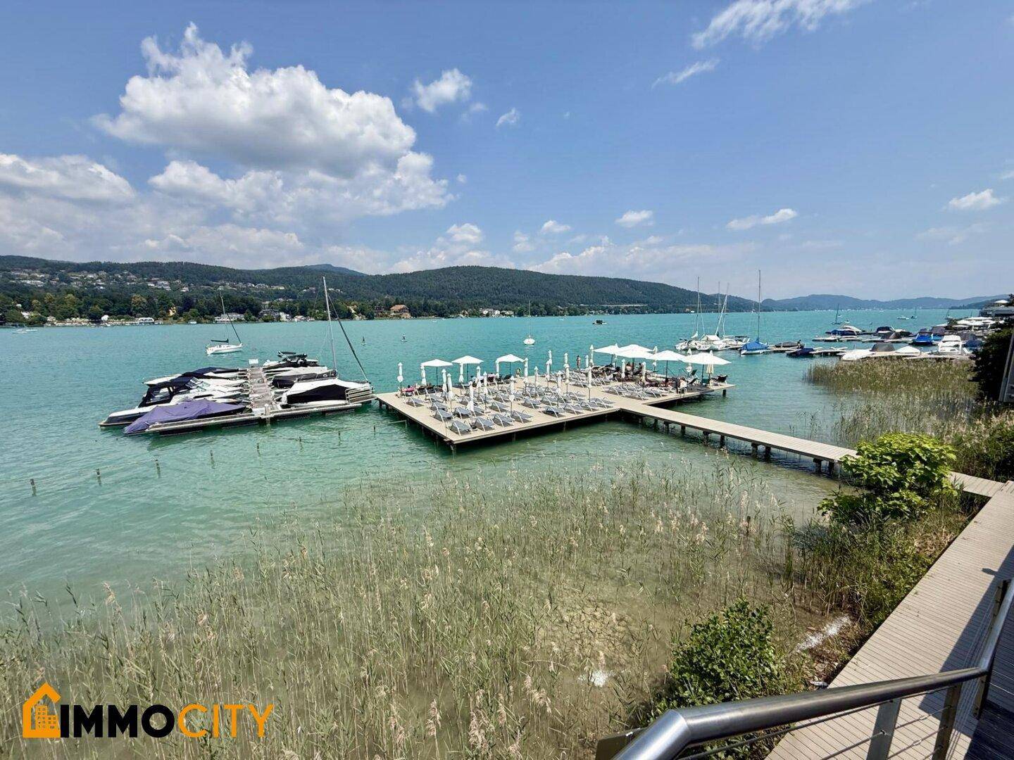 Weitläufiger Blick von einem Balkon auf den See mit schwimmender Plattform und zahlreichen Booten.