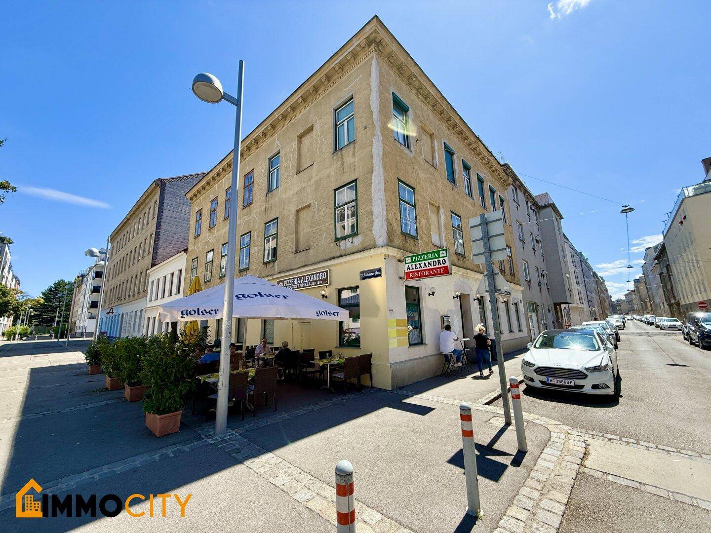 Weitläufige Eckansicht des Gebäudes mit dem Restaurant und der belebten Straße an einem sonnigen Tag.