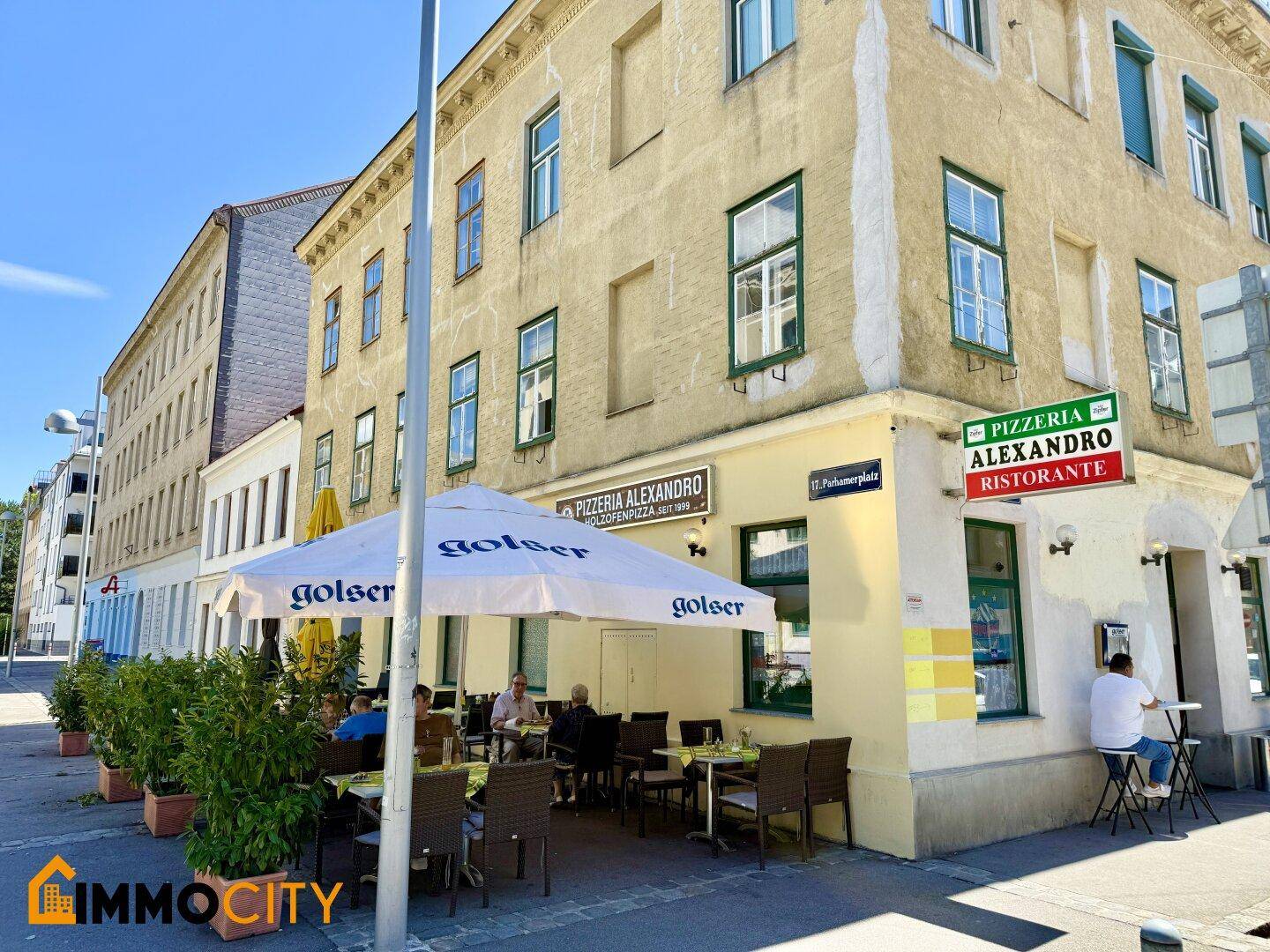 Eckansicht des Gebäudes mit dem Restaurant und seiner Außenterrasse an einem sonnigen Tag.