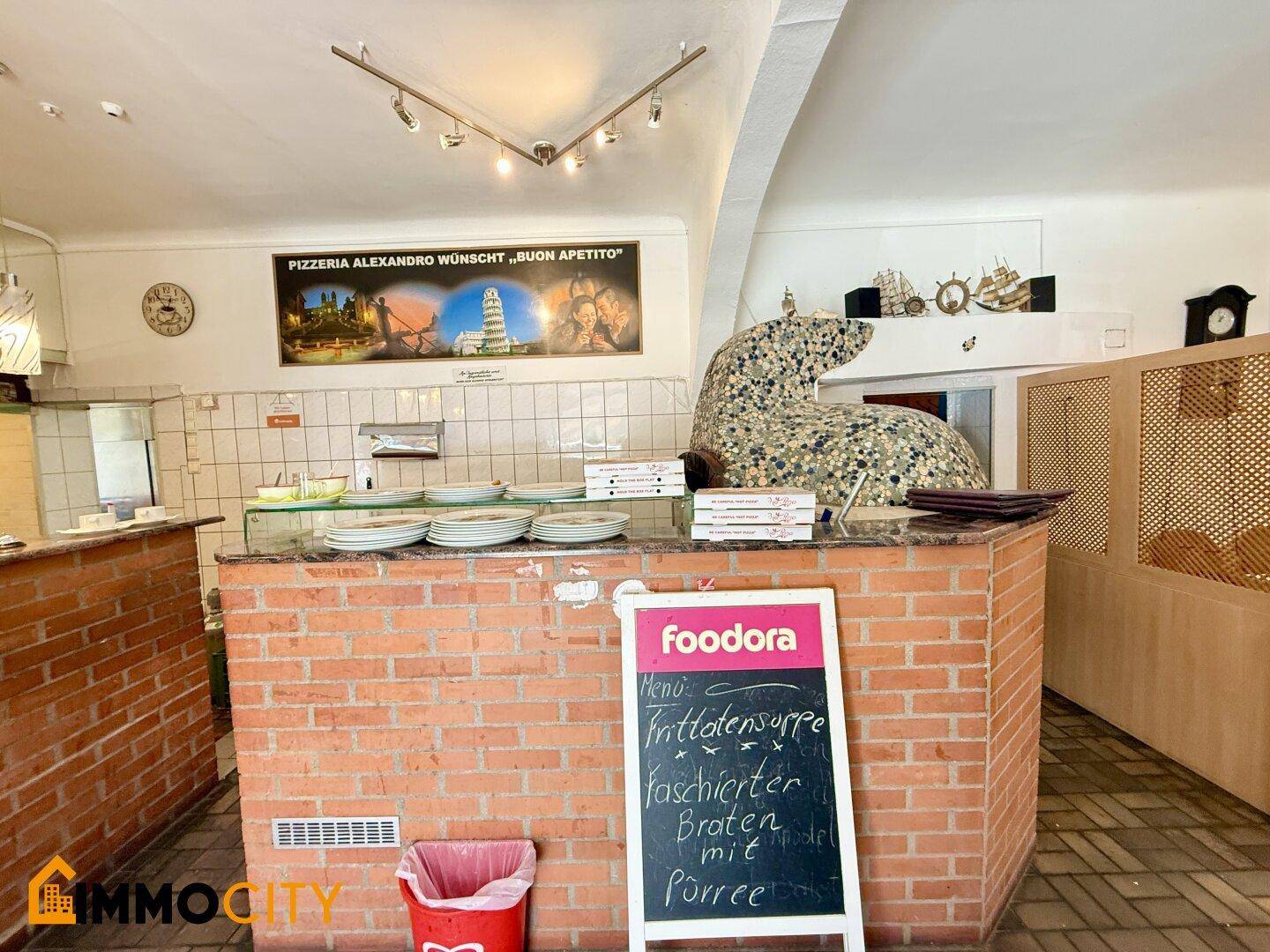 Thekenbereich des Restaurants mit einer Speisekarte und dem kunstvoll gestalteten Pizzaofen im Hintergrund.