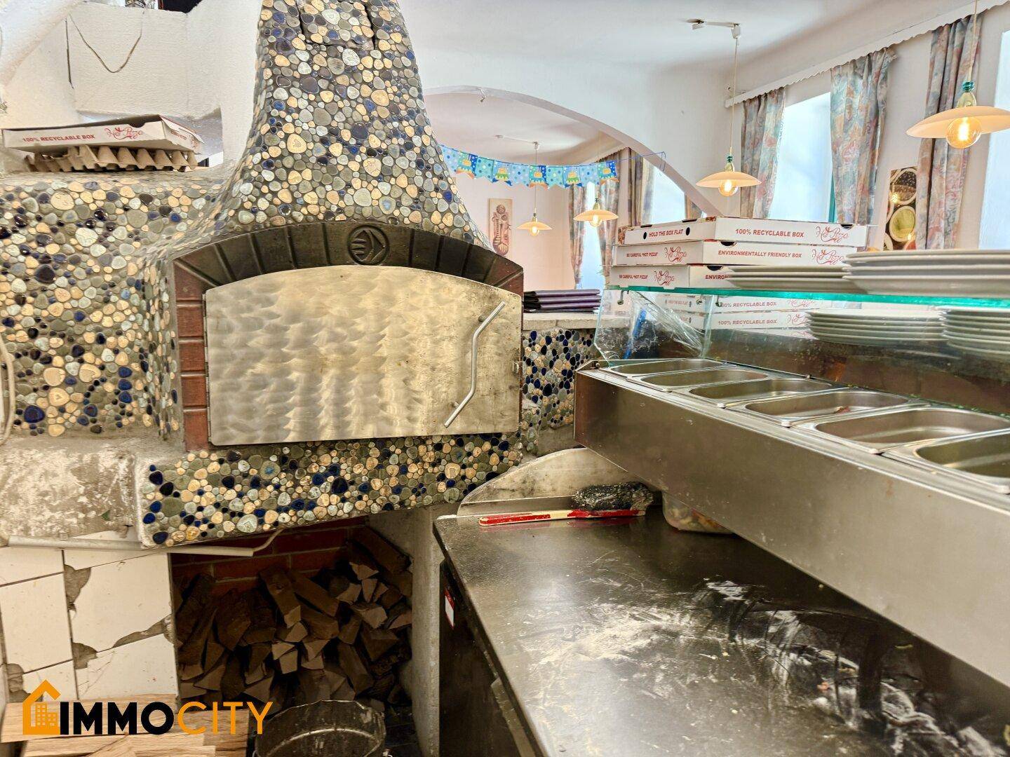 Nahaufnahme eines kunstvoll gefliesten Pizzaofens mit einem Arbeitsbereich und Holzscheiten darunter.