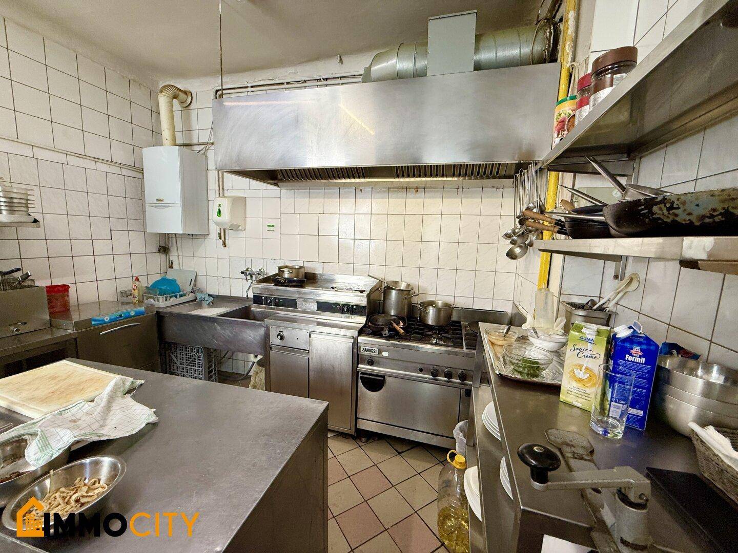 Professionelle Restaurantküche mit Edelstahlgeräten, gefliesten Wänden und einer großen Dunstabzugshaube.
