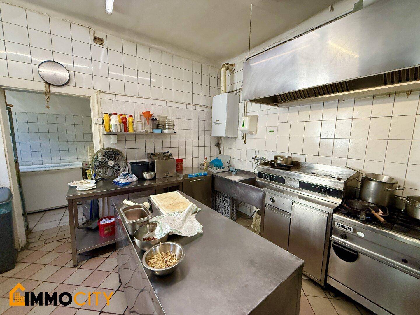 Professionelle Restaurantküche mit Edelstahlgeräten, gefliesten Wänden und einer großen Dunstabzugshaube.