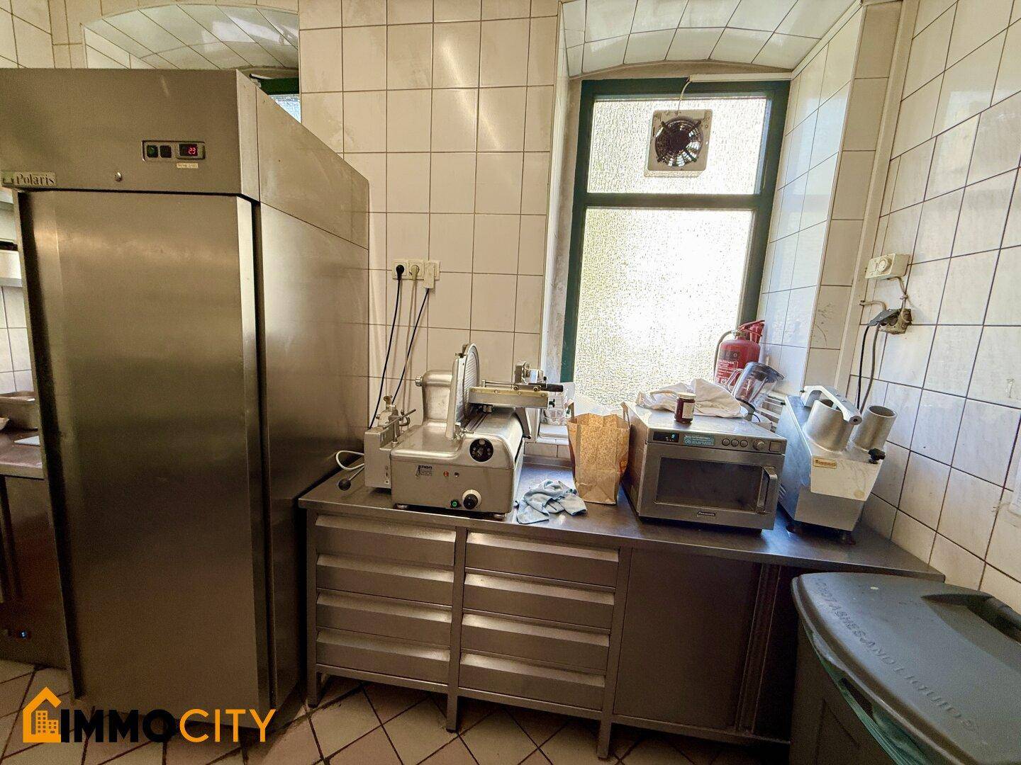 Gewerbliche Küche mit einem großen Edelstahlkühlschrank, Schneidemaschine und weiteren professionellen Geräten.