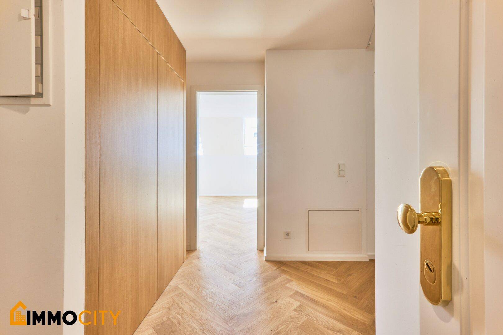 Heller Flur mit elegantem Fischgrätparkett und integrierten Holzschränken, der zu weiteren Räumen führt.