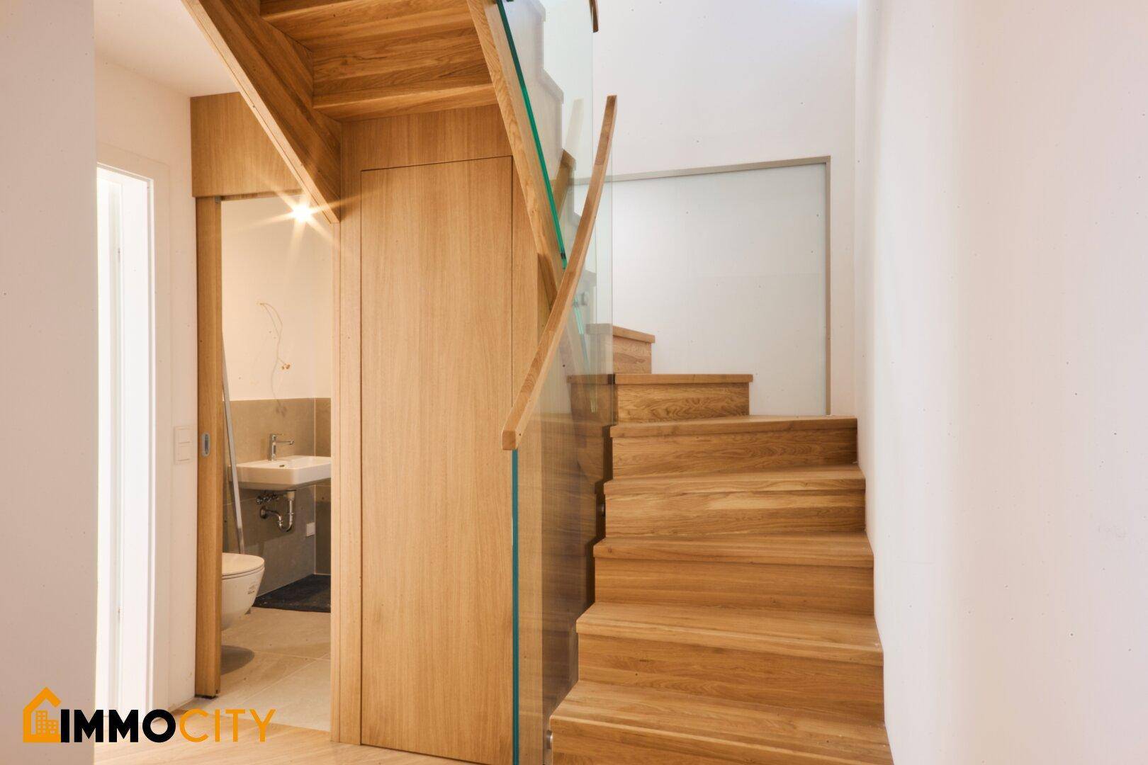 Moderne Holztreppe mit Glasgeländer und Blick auf ein stilvolles Gäste-WC mit Waschbecken und Toilette.
