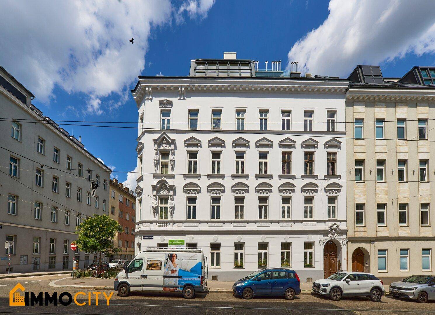 Historisches Eckgebäude mit klassischer Architektur und moderner Dachaufstockung an einer städtischen Straße.
