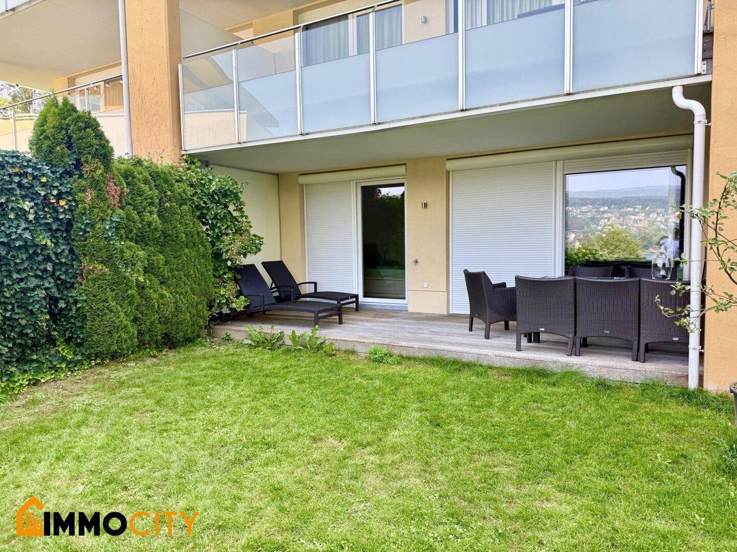 Gepflegter Gartenbereich mit Holzterrasse, Liegestühlen und Essgruppe unter einem Balkon.