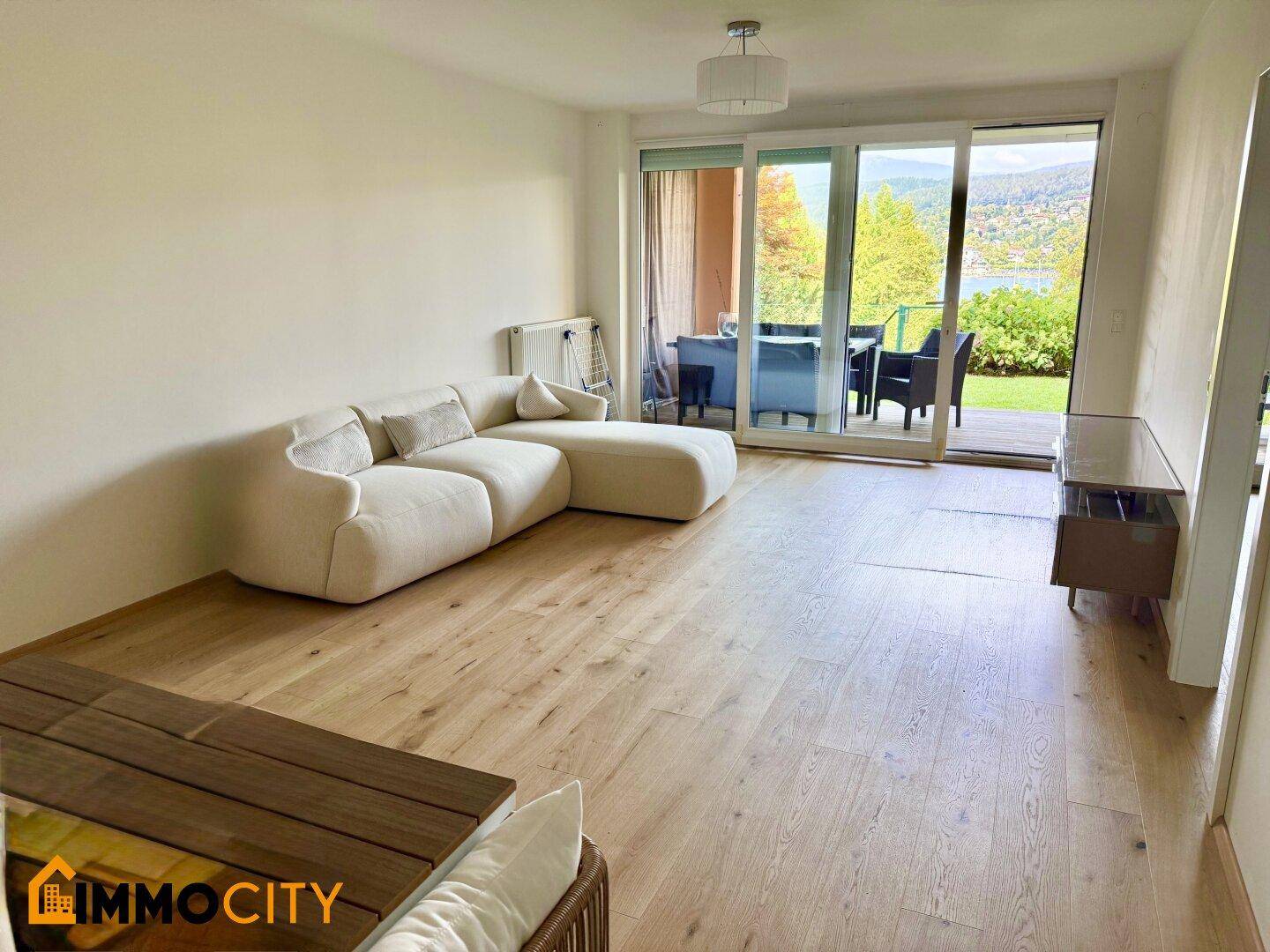 Helles Wohnzimmer mit modernem Sofa, Holzboden und Zugang zur Terrasse mit Seeblick.