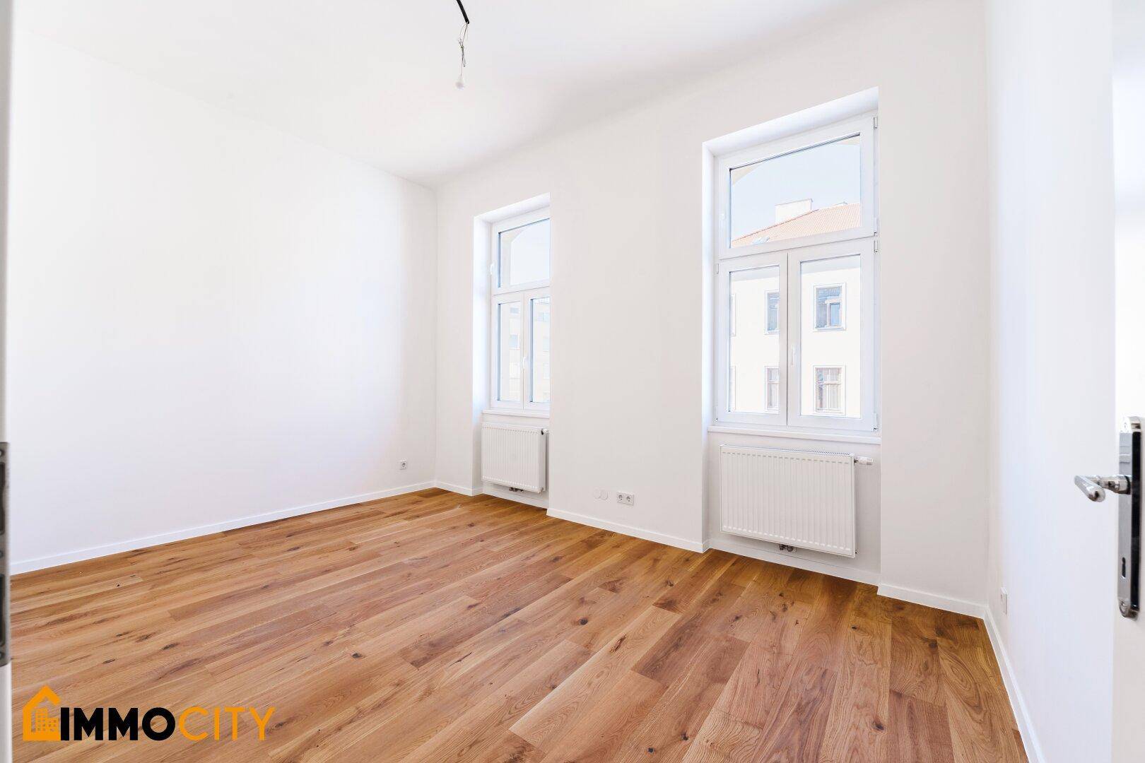 Lichtdurchflutetes Zimmer mit Parkettboden und zwei Fenstern, bereit zum Einzug.