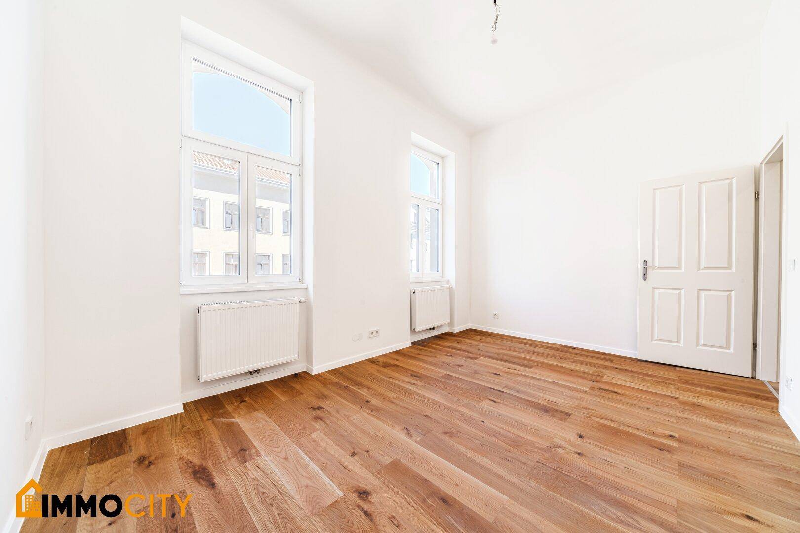 Geräumiges Zimmer mit Holzboden und hohen Fenstern, ideal als Schlaf- oder Wohnzimmer.