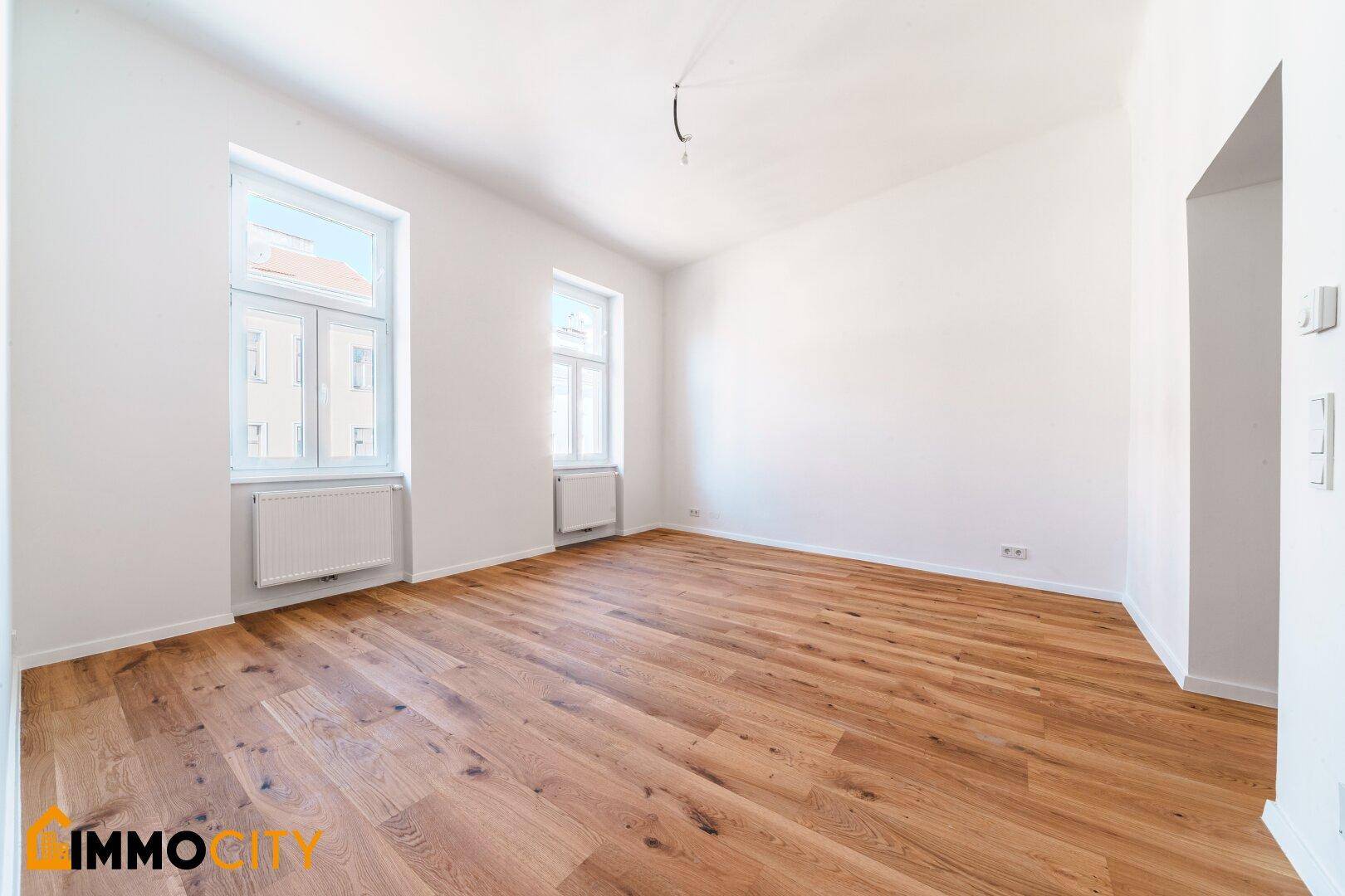 Geräumiges Zimmer mit Parkettboden und zwei großen Fenstern, bietet viel Tageslicht.