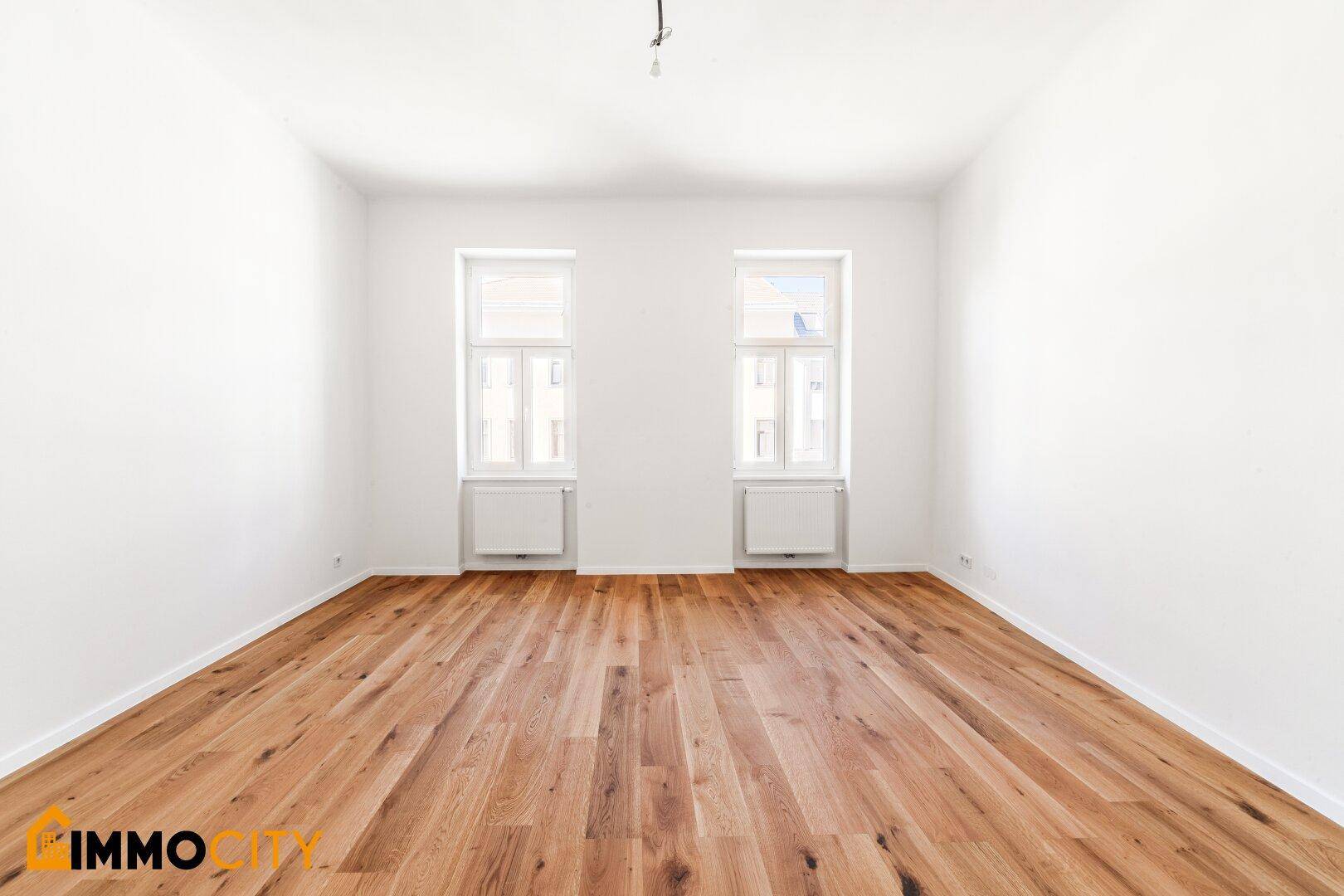 Helles, leeres Zimmer mit Parkettboden und zwei Fenstern, ideal für Schlaf- oder Wohnbereich.