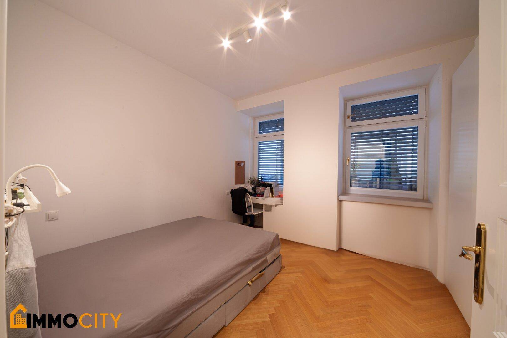 Gemütliches Schlafzimmer mit Parkettboden, Einzelbett und Schreibtisch am Fenster.