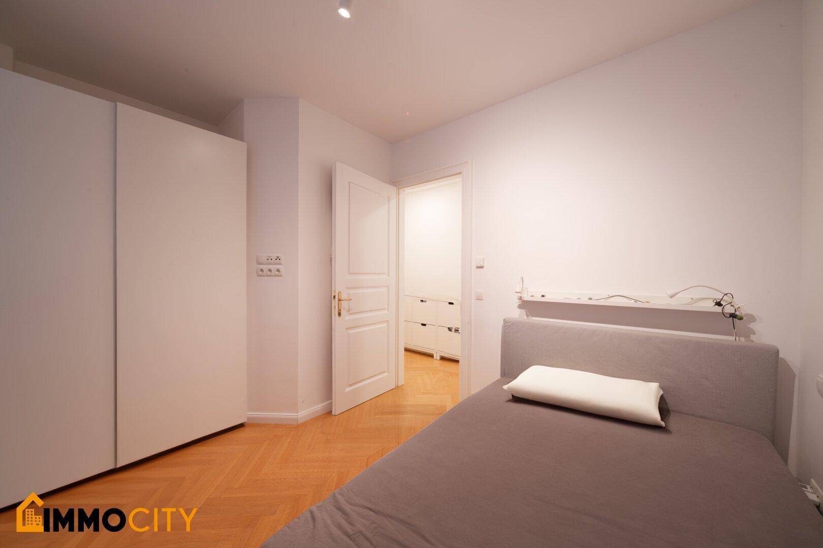 Schlafzimmer mit Parkettboden und großen weißen Einbauschränken, die viel Stauraum bieten.
