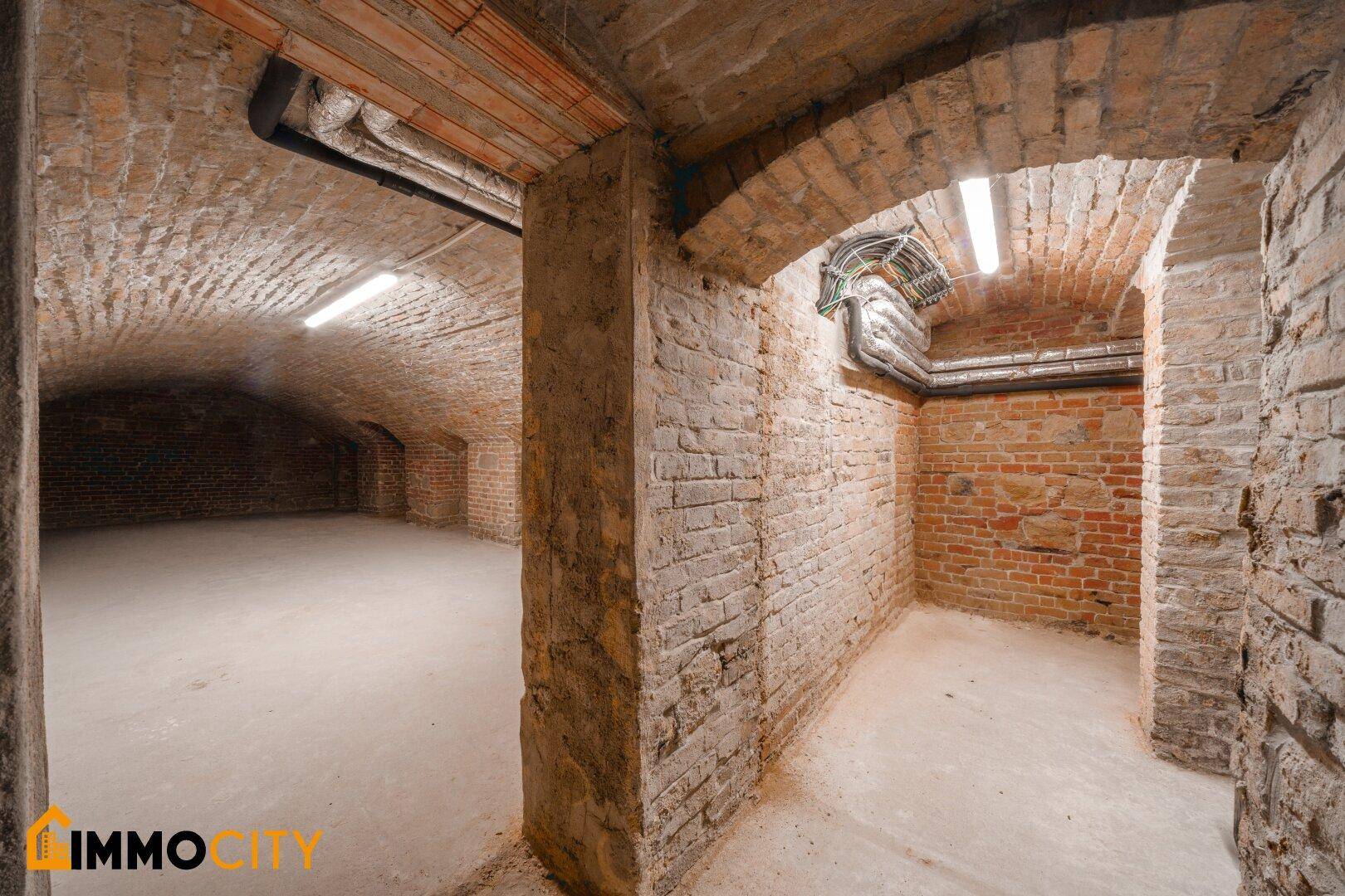 Tiefer Gewölbekeller mit freiliegenden Ziegeln und sichtbaren Rohren an der Decke.