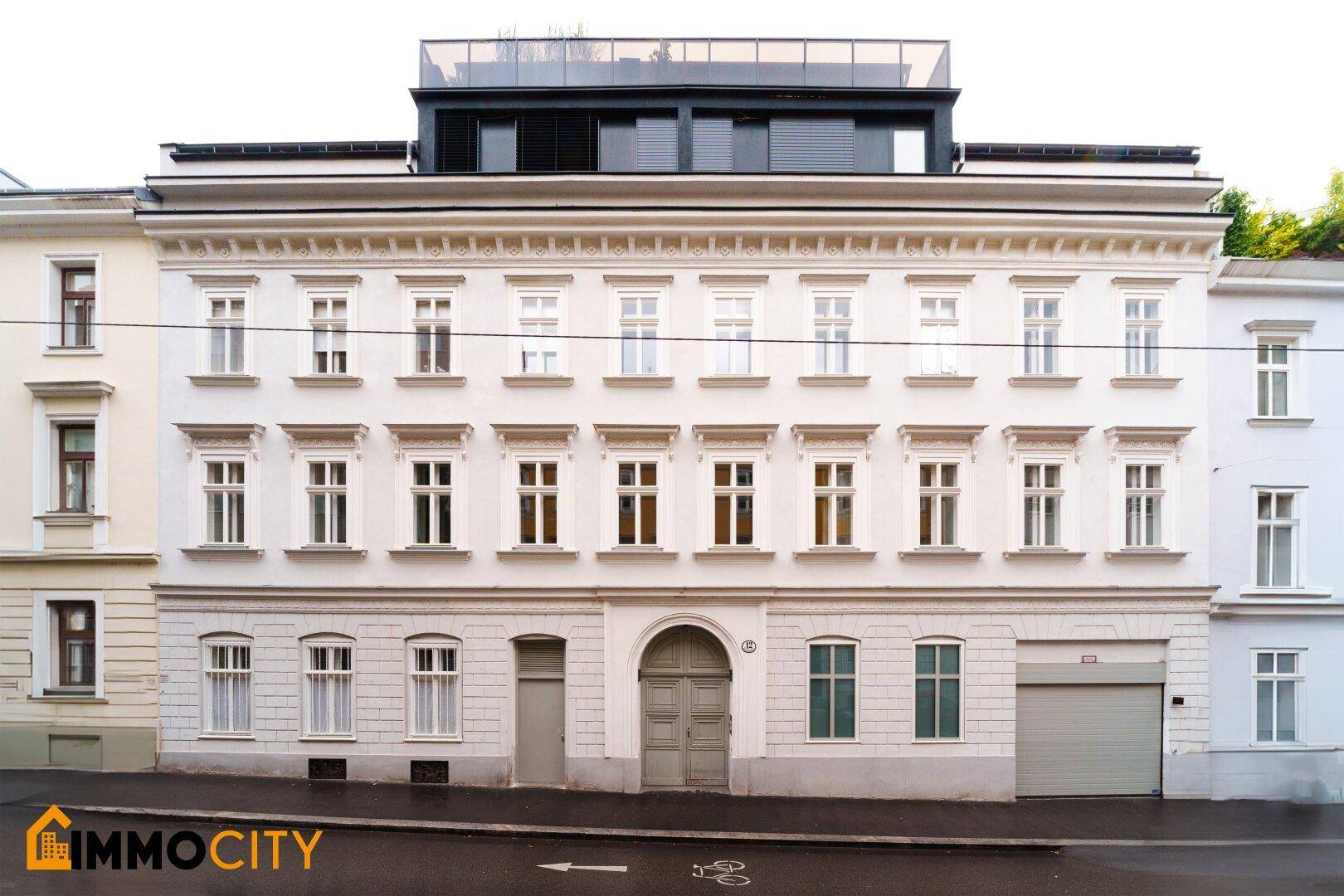 Klassische Altbaufassade mit vielen Fenstern und einem modernen Dachaufbau.