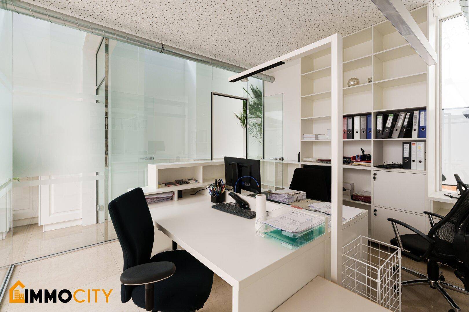 Heller Büroraum mit Glaswänden, integriertem Regal und modernem Arbeitsplatz.