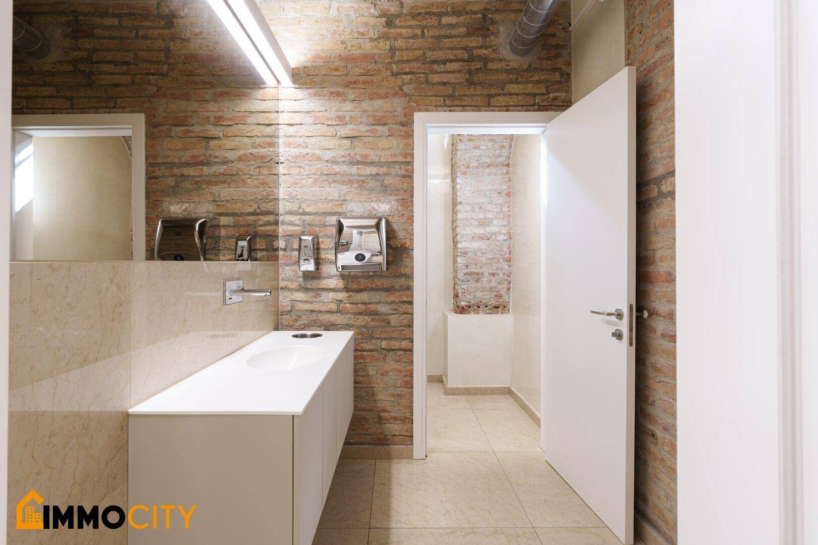 Modernes Badezimmer mit freiliegender Backsteinwand, elegantem Waschtisch und Handtrocknern.