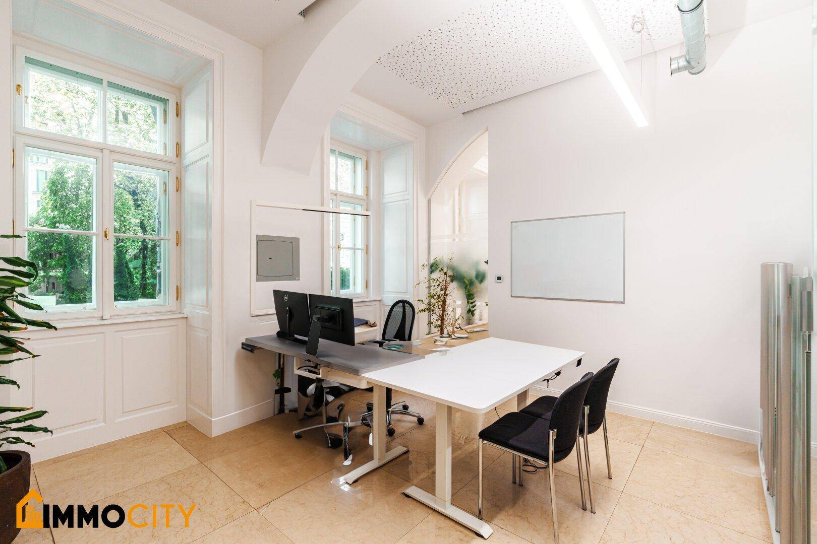 Heller Bürobereich mit zwei Arbeitsplätzen, großen Fenstern und Blick ins Grüne.