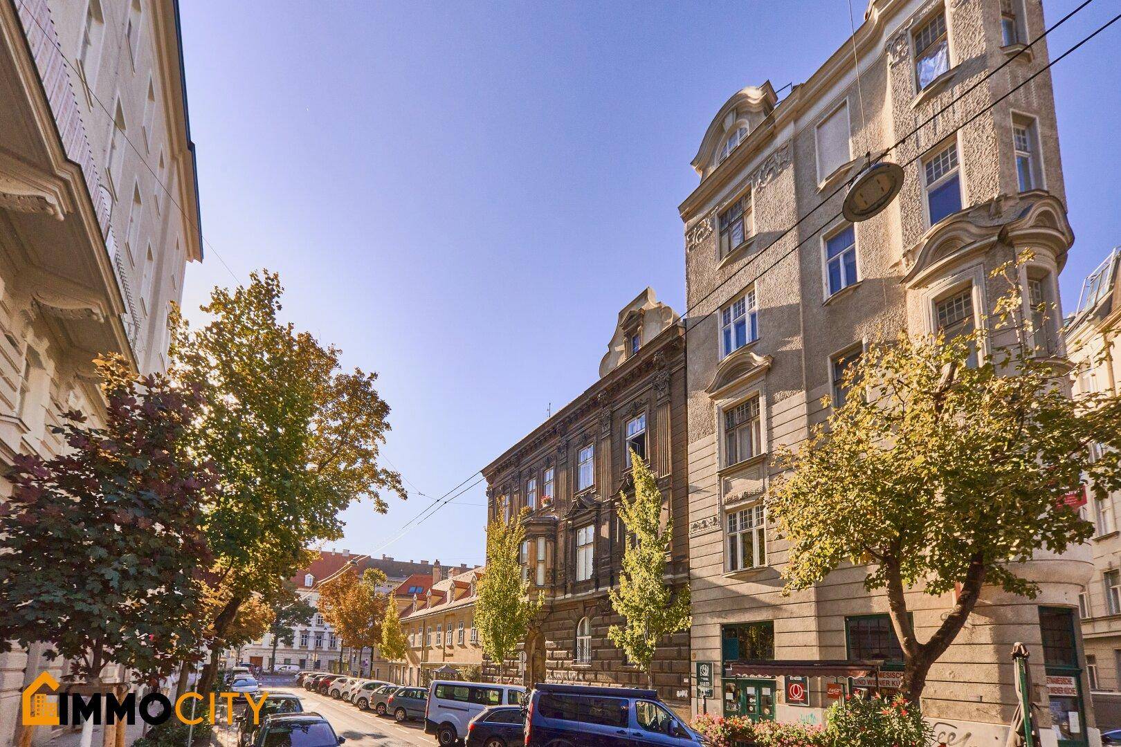 Historisches Gebäude an einer ruhigen Straße mit parkenden Autos und Bäumen.