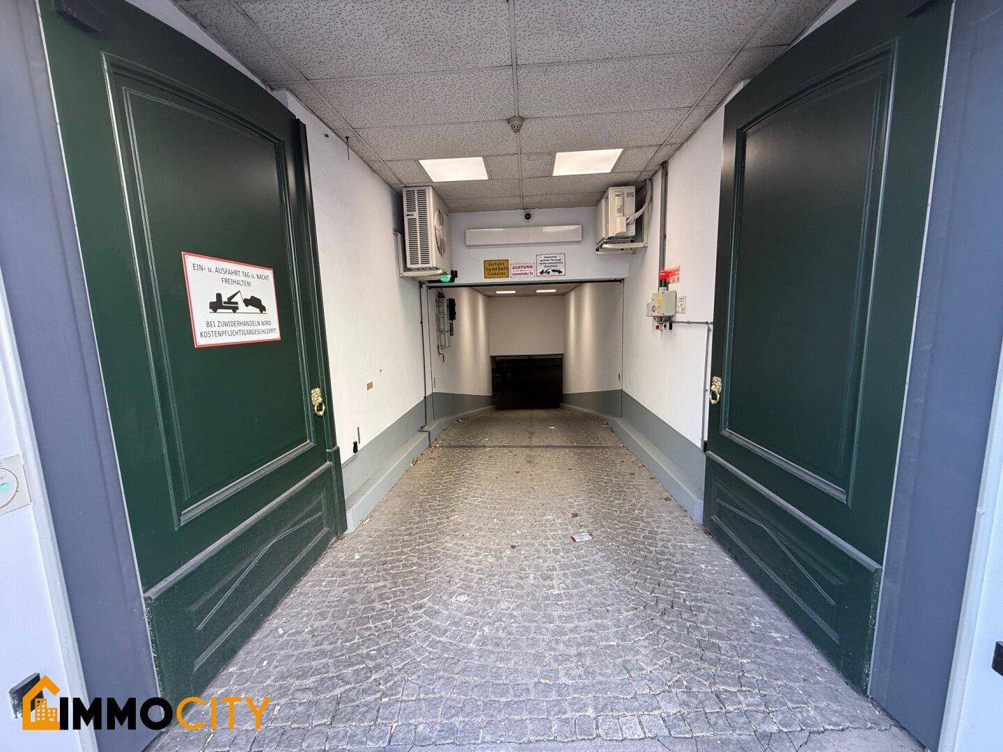 Eingang zu einer Tiefgarage mit großen grünen Toren und einer gepflasterten Rampe.