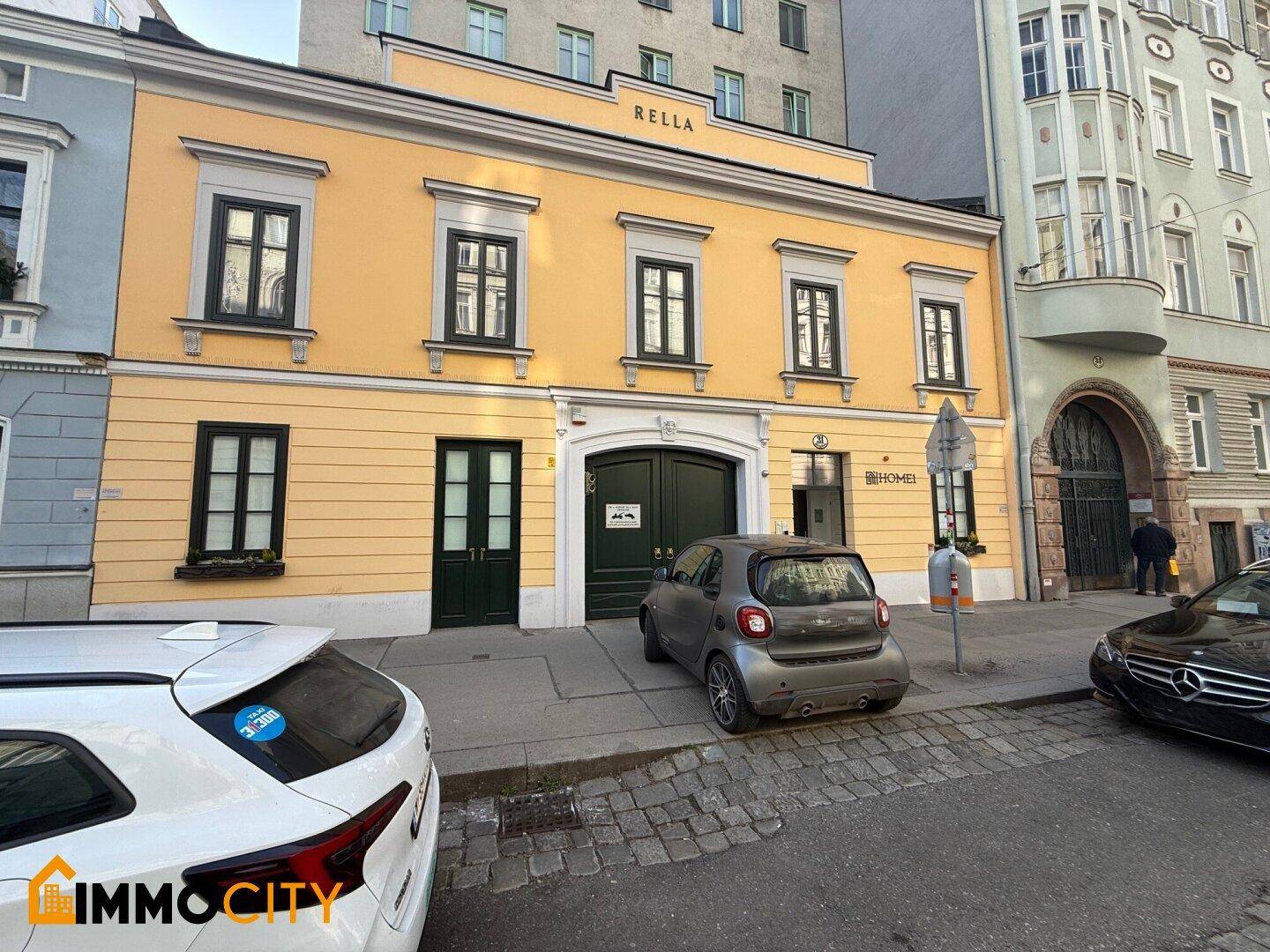 Historisches gelbes Gebäude mit grünen Türen und Fenstern an einer belebten Stadtstraße.
