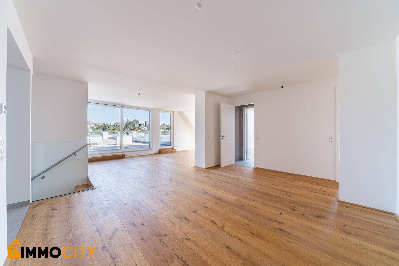 Offener Wohnbereich mit Holzfußboden, viel Tageslicht und einer modernen Treppe mit Glasgeländer.