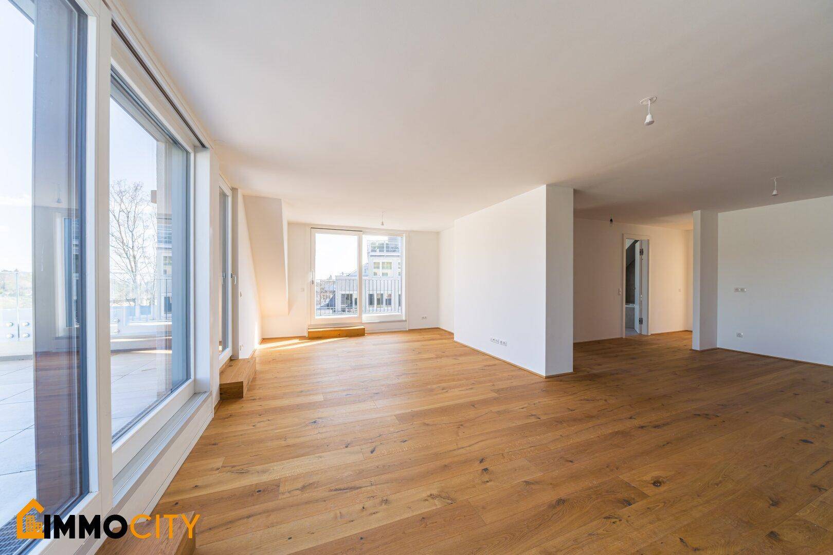 Heller Wohnraum mit breiten Fensterfronten, Holzboden und Zugang zu den Außenbereichen.