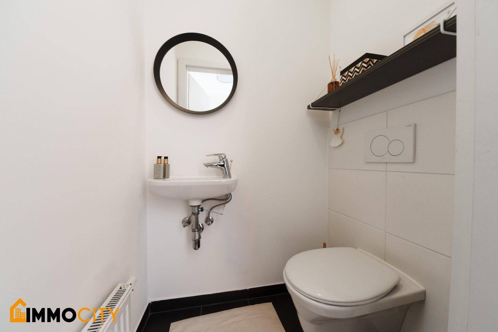 Modernes Gäste-WC mit Wand-WC, kleinem Waschbecken und Spiegel.
