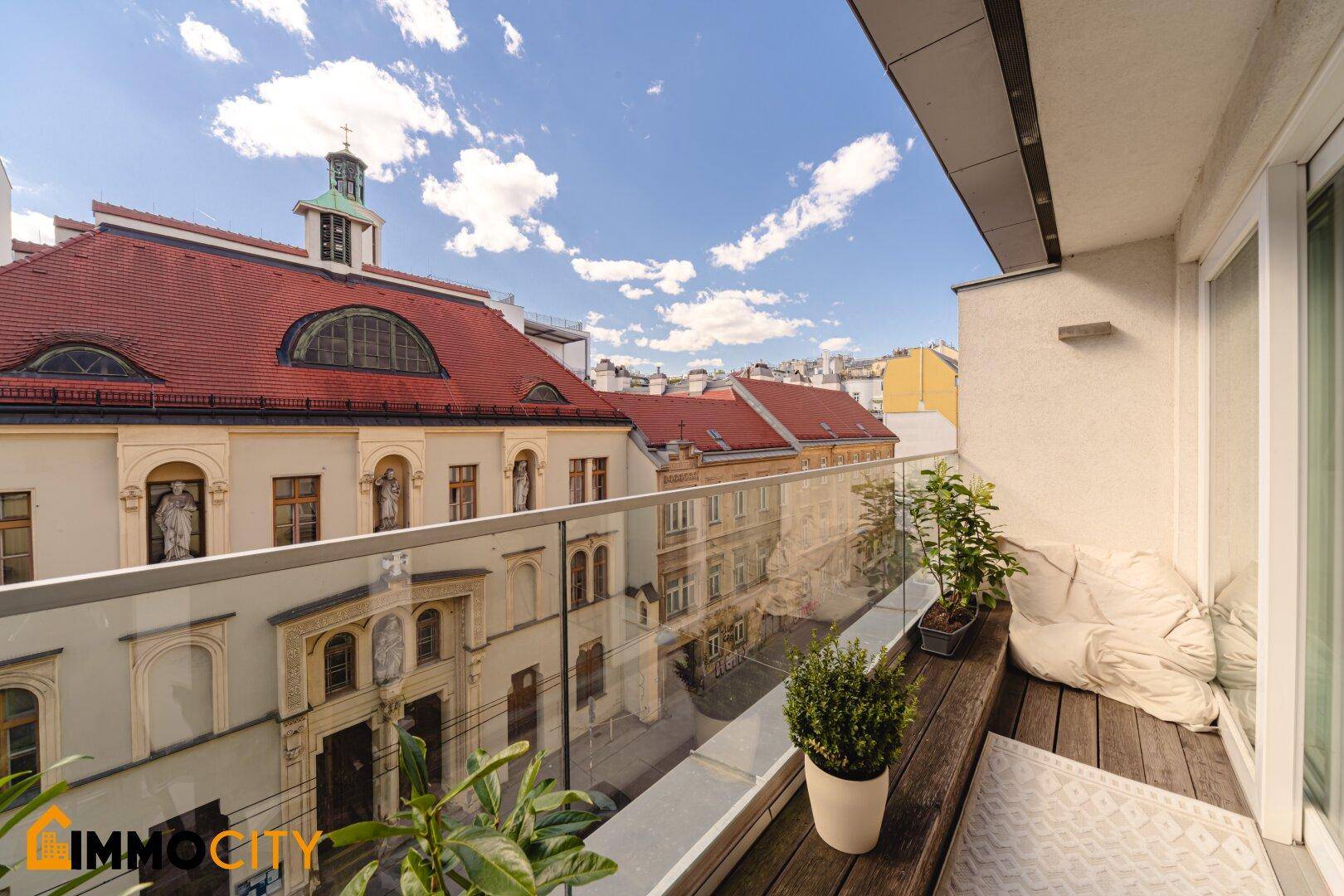 Balkon mit Glasgeländer und weitem Blick über die Dächer der Stadt.