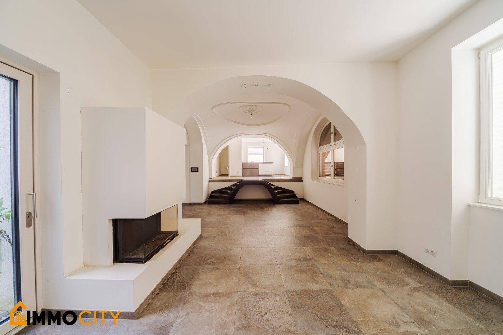 Helles Wohnzimmer mit eleganten Gewölbedecken, integriertem Kamin und Blick auf den erhöhten Bereich.