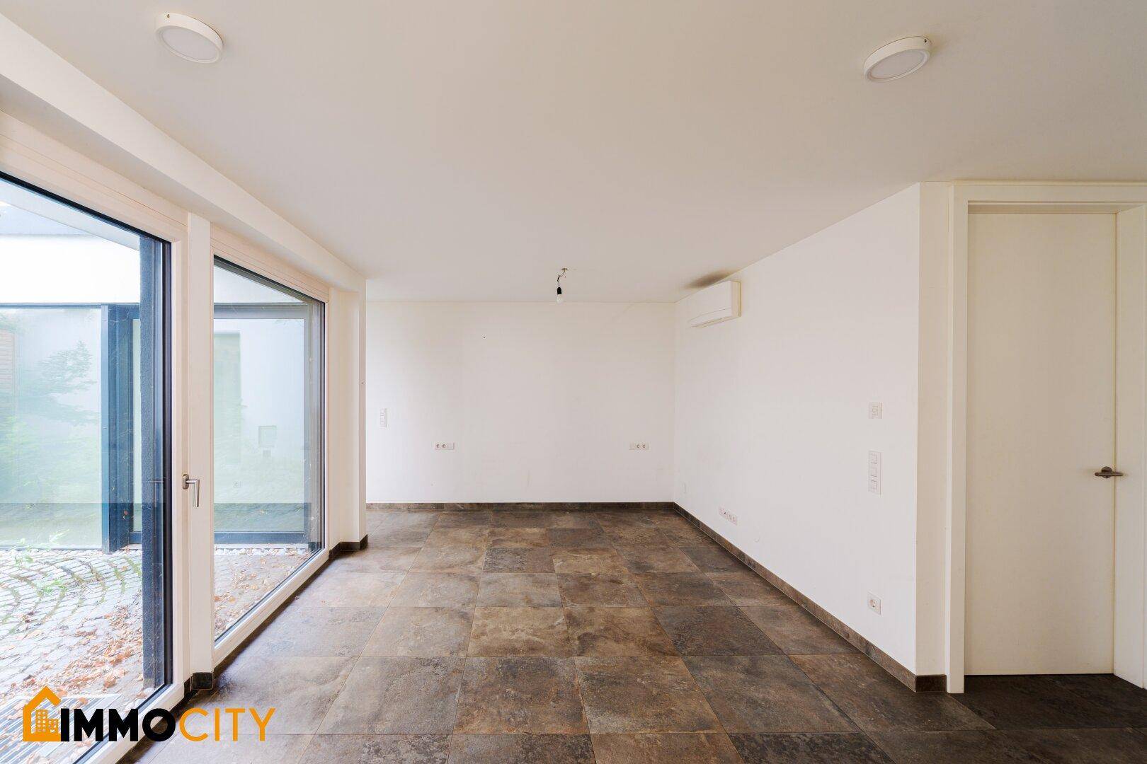 Helles Zimmer mit großen Glasschiebetüren, die viel Tageslicht hereinlassen und zum Innenhof führen.