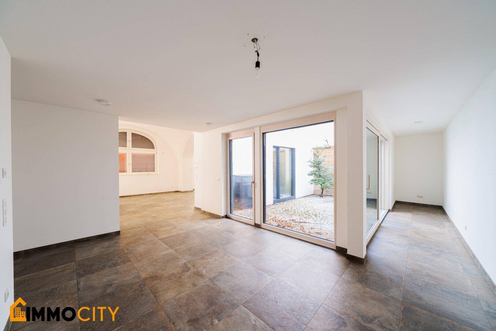 Helles Wohnzimmer mit großen Glasschiebetüren, die den Blick auf den gepflasterten Innenhof freigeben.