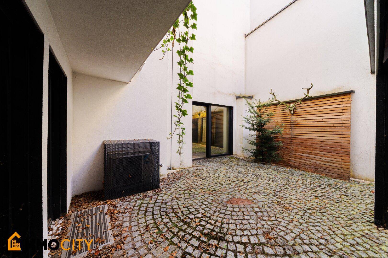 Gepflasterter Innenhof mit Kletterpflanzen, einem kleinen Baum und rustikaler Wanddekoration.
