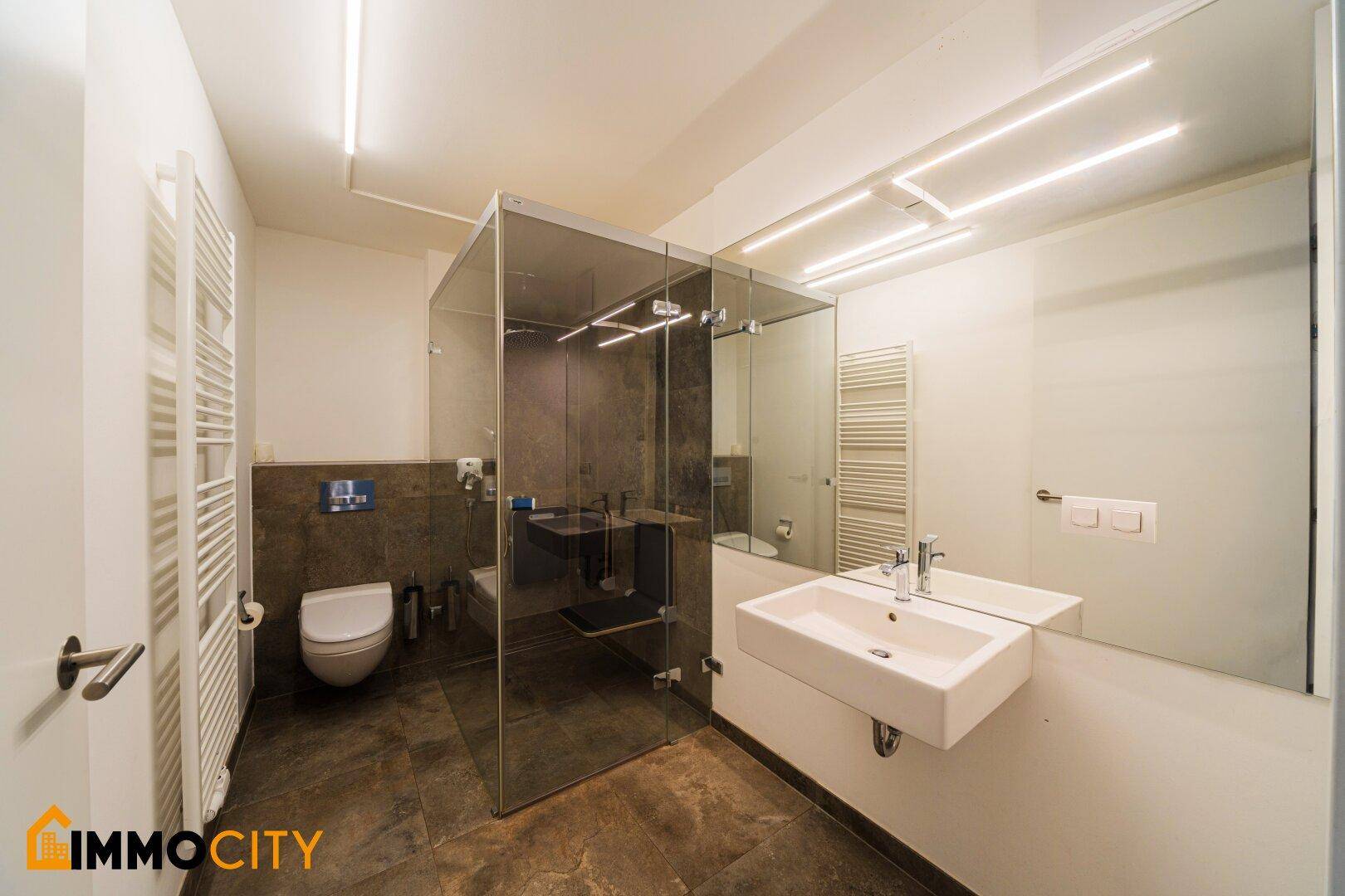Modernes Badezimmer mit begehbarer Dusche, wandhängendem WC und beheiztem Handtuchhalter.