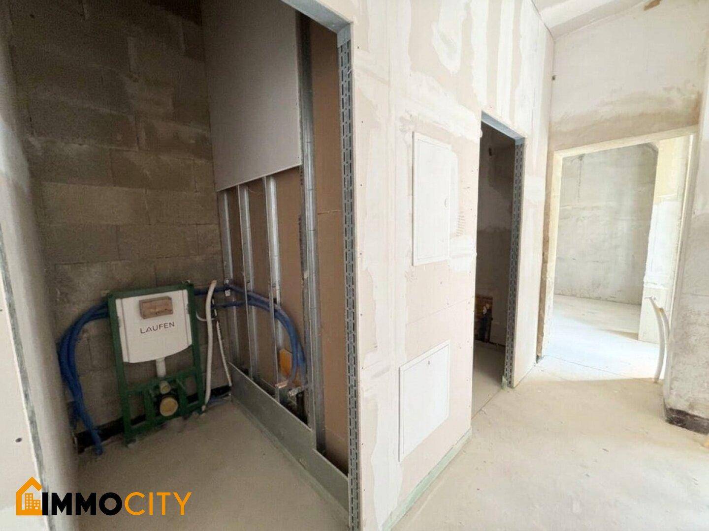 Unfertiges Badezimmer mit sichtbaren Sanitärinstallationen für eine Wandtoilette und Trockenbauwänden.