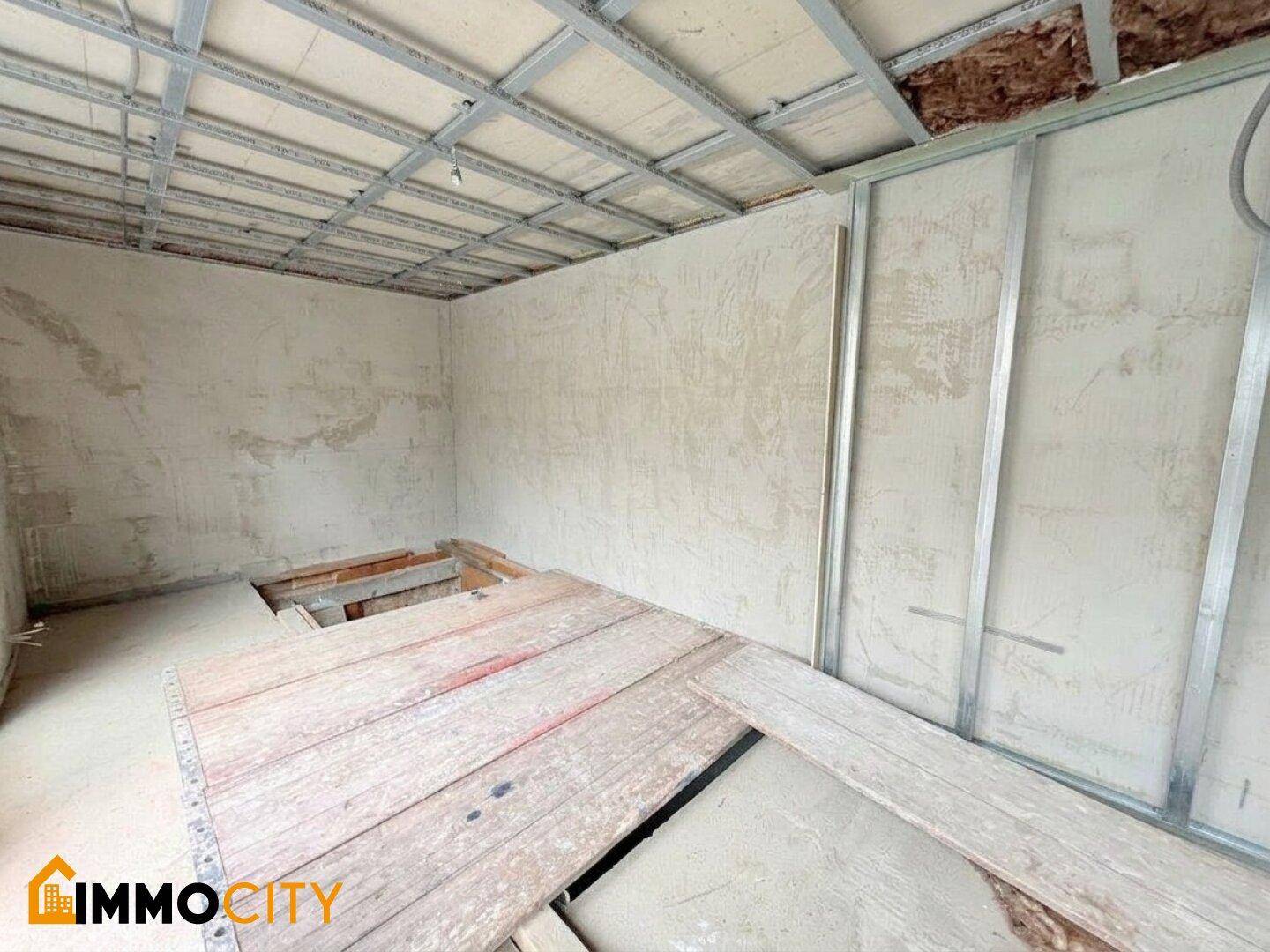 Unfertiger Raum mit sichtbarer Deckenkonstruktion und teilweise freigelegtem Holzboden, der auf Renovierung wartet.