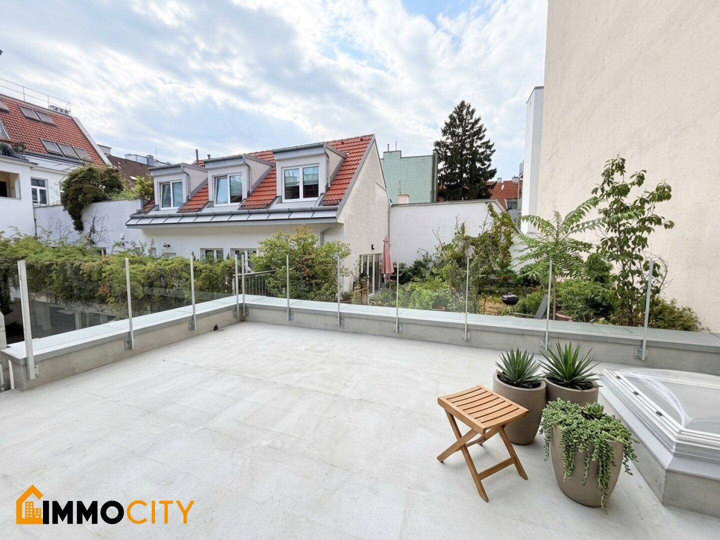 Geräumige Dachterrasse mit Glasgeländer, Topfpflanzen und Blick auf umliegende Gebäude und Gärten.